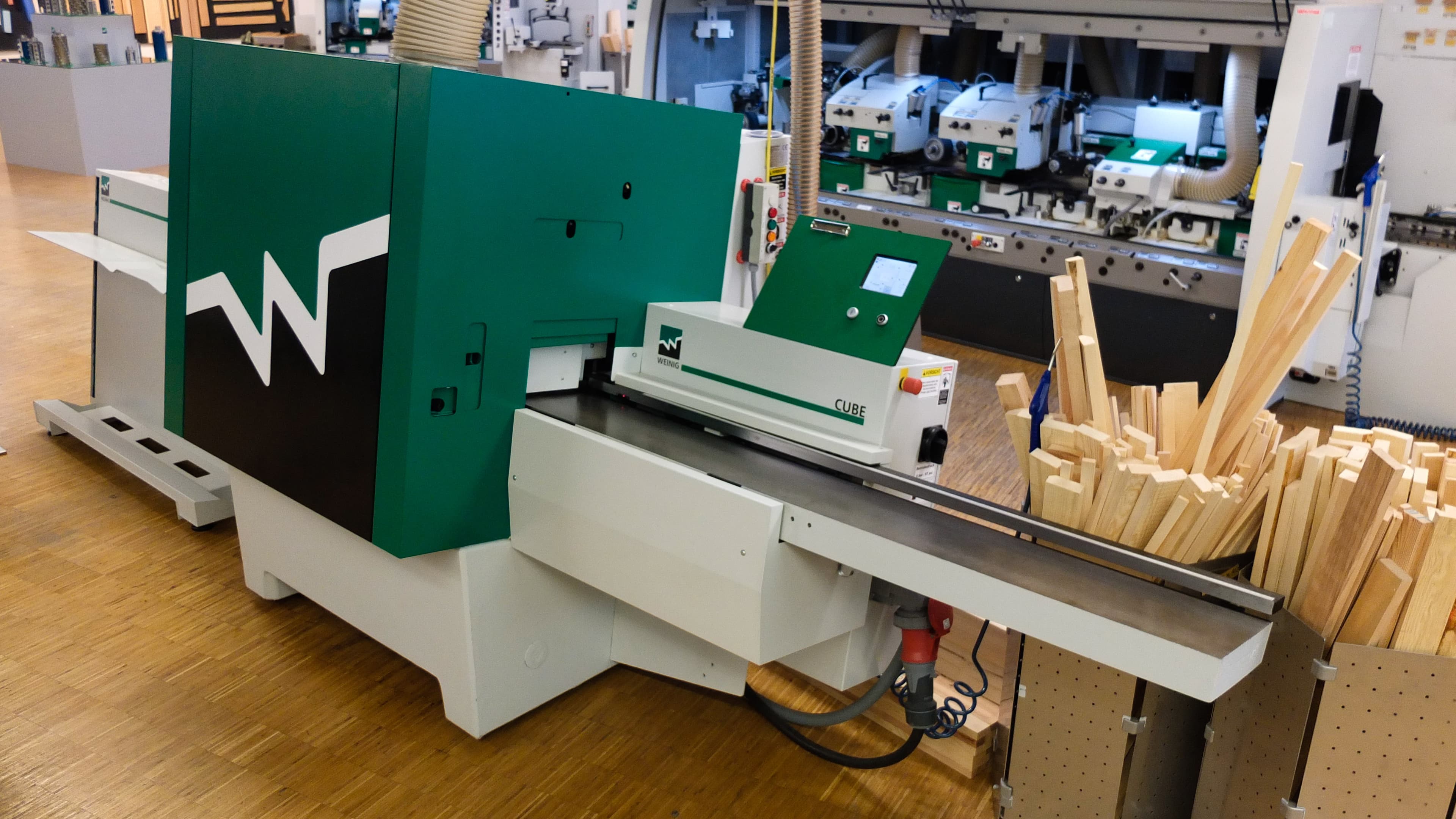 Weinig Cube four-sided industrial planer machine on a factory floor, showing the full infeed and outfeed section of a modern high-speed moulder planer